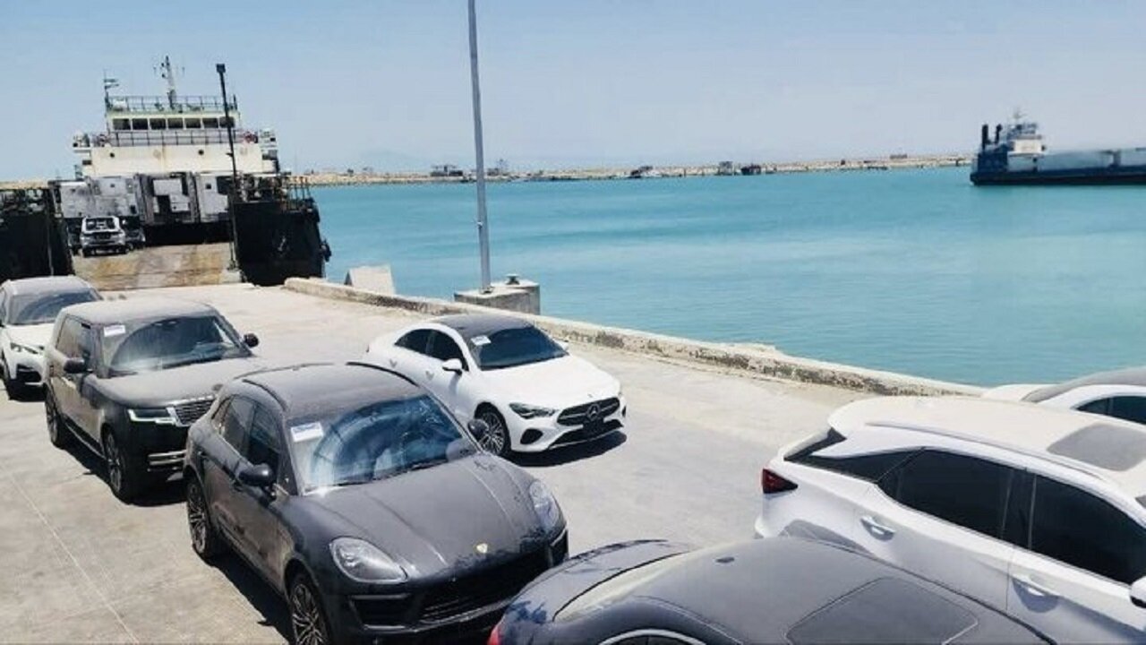 تصویری از شناور لندینگ‌کرافت در حال تخلیه خودروهای سبک در اسکله بندر جاسک، با نمایش بخشی از منطقه بندری و فعالیت‌های لجستیکی.